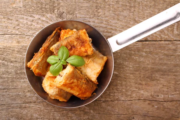 bir tavada kızarmış balık hake fesleğen ile dekore edilmiştir.