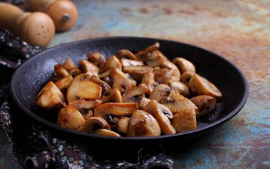 Siyah tavada kızartılmış mantarlar, kırsal bir zemin.