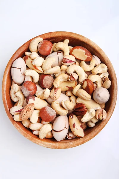 Mix nuts in a woden bowl on a white backround . Cashew, hazelnuts, walnuts, pistachio, pecan, brazilian nuts and peanuts. Top view.
