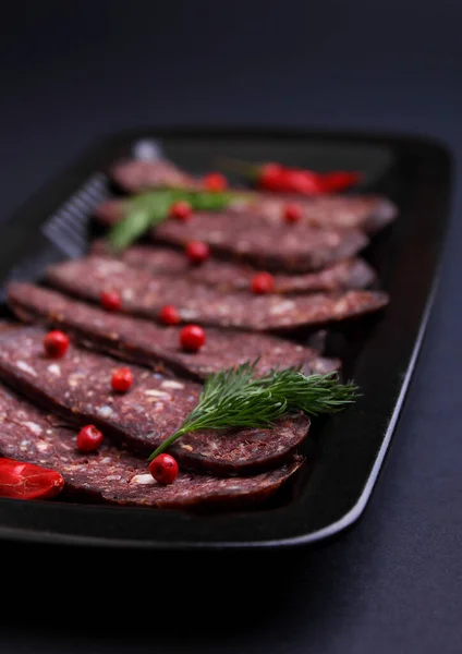 Cured meat cut into slices in a black plate on a black background