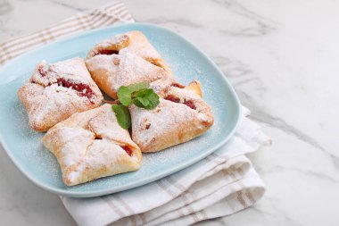 Şeker tozuyla süslenmiş reçelli çörek ve mermer zemin üzerinde nane.