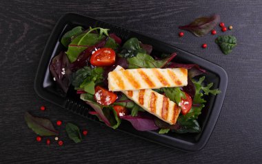 Koyu arka planda beyaz tabakta kızarmış halloumi peynirli yeşil salata.