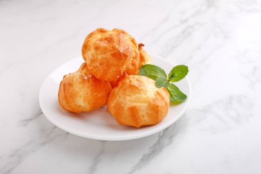 Kremalı profiteroller mermer arka planda naneyle süslenmiş.