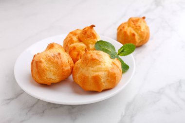 Kremalı profiteroller mermer arka planda naneyle süslenmiş.