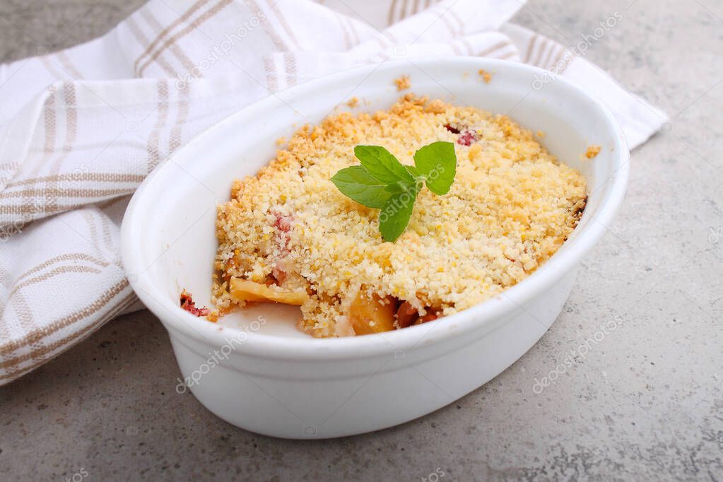 Crumble with strawberries and apples on a white plate and concrete background.