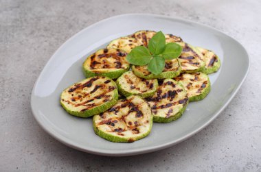 Kabak dilimlenmiş ve ızgarada kızartılmış. Fesleğenle süslenmiş..