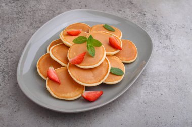 Çilekli bir tabakta krep. Beton bir arka planda naneyle süslenmiş.