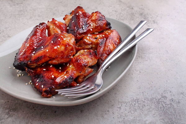 Grilled chicken wings in soy sauce decorated with sezame in a plate on a concrete background