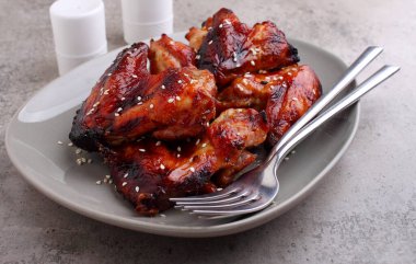 Soya soslu ızgara tavuk kanadı. Beton bir arka planda fesleğenle süslenmiş.