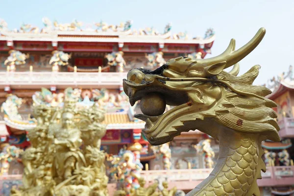 Golden dragon with its eye scorched and its mouth holding a golden ball. Chinese temple is in the background.