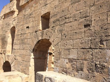 Duvar, antik Roma duvarları, Tunus 'taki amfi tiyatronun kalıntıları. Korunmuş kemerler, pencereler. Duvarda ahşap yapıların bağlanma izleri var. Sarımsı yapı taşları pürüzsüzce yapılmış. Keskin gölgeler.