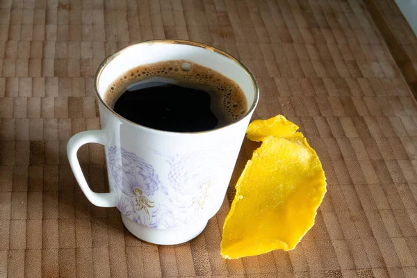 A cup of coffee and a slice of dried mango