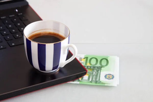  Dizüstü bilgisayarda bir fincan kahve ve 100 avroluk banknotlar. İnternetten kazanç, uzaktan çalışma.