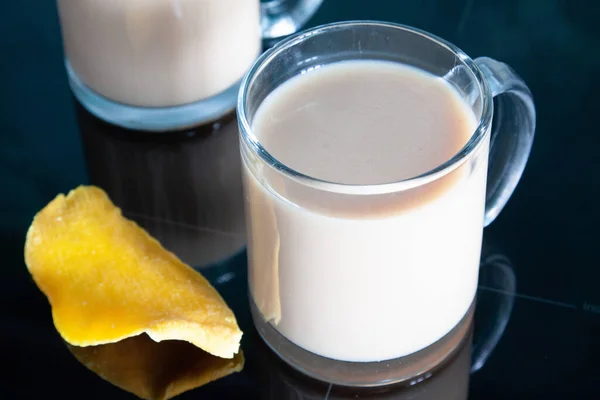 ミルクティーのグラス2杯を背景に 光沢のある暗い表面に乾燥マンゴーのスライス — ストック写真
