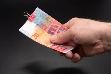 Bir el, 20 franklık bir deste İsviçre banknotunu pembe bir ataçla tutuyor.
