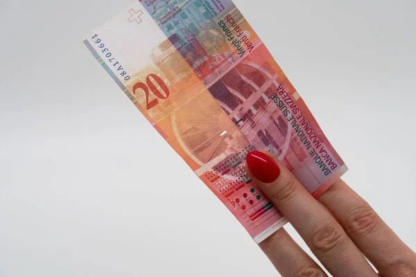 Female fingers holding a Swiss banknote of twenty francs, diagonal