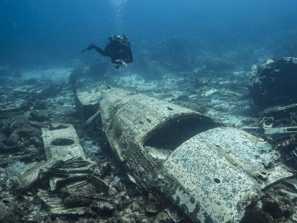 Airplane wreck as part of coral reef in Caribbean Sea around Curacao with blue background and diver