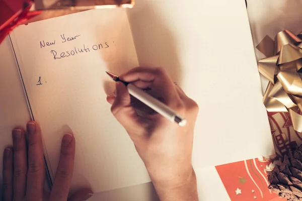 Nyårslöften som skrivs med en hand på anteckningsboken med nyår dekorationer — Stockfoto