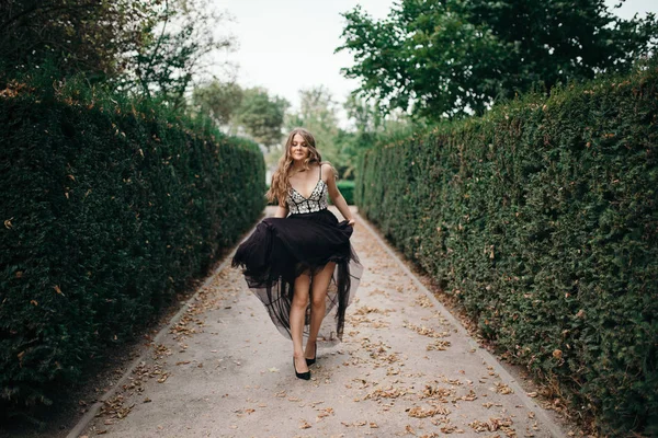 Vacker kvinna i lång svart aftonklänning gå väg i park — Stockfoto