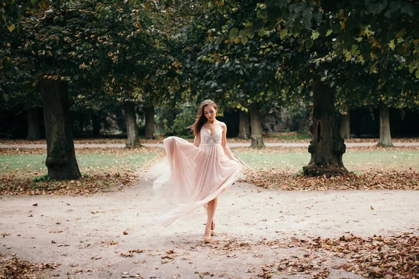 Beautiful woman in long rose evening dress walking path in park. — Stock Photo, Image