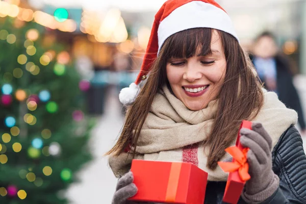 Beautiful woman in santa hat holding present box onchristmas market — Stock Photo, Image