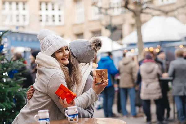 two girls best friends giving presents on christmas market