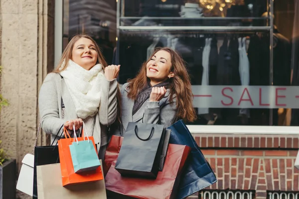 Dos chicas están contentas con una compra delante de la venta de texto —  Fotos de Stock