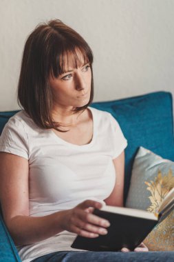 Güzel bir kadın evde kitap okuyor.