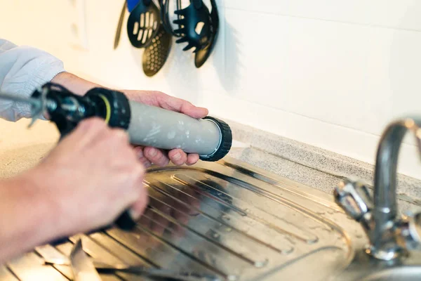 Manos de trabajador usando un tubo de silicona para reparar en la cocina —  Fotos de Stock