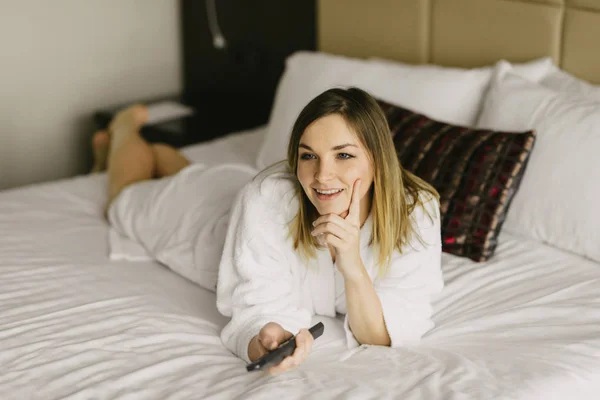 Hermosa mujer acostada en la cama y ver la televisión en la habitación de hotel —  Fotos de Stock