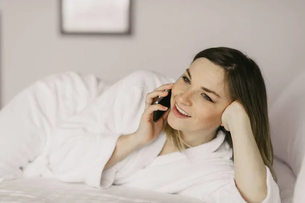 Vacker kvinna liggande på sängen och sett på din smartphone i hotel — Stockfoto