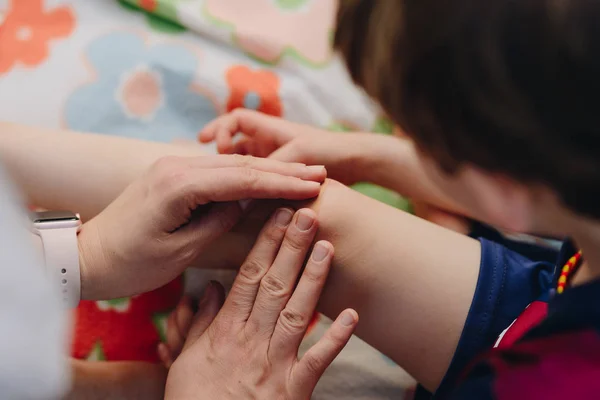 Wunde am Knie des Kindes schließen. Mutter kleidet Kind in die Knie. — Stockfoto