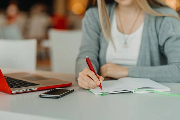 Handen van vrouwelijke schrijven op notebook in café met laptop, smartphone en kopje koffie — Stockfoto