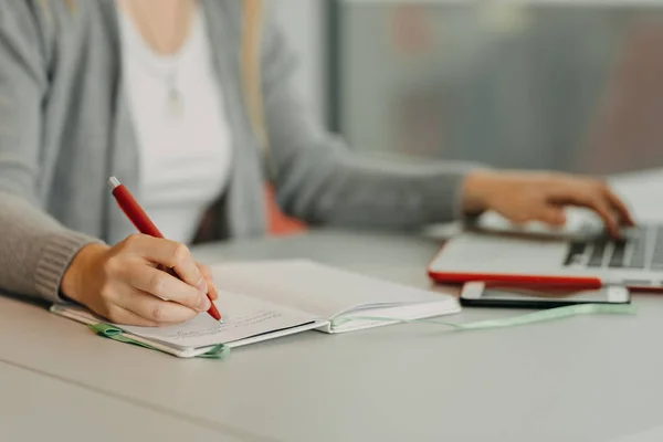 Mani di scrittura femminile su notebook in caffè con computer portatile, smartphone e tazza di caffè — Foto Stock