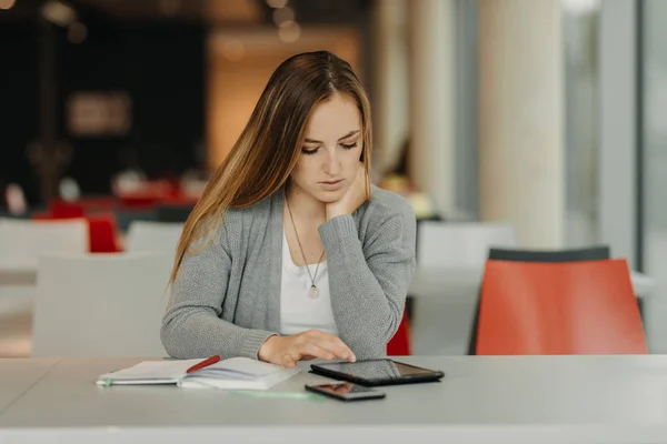 Ganska kvinnlig student med smartphone och surfplatta lärande i en Gymnasiebiblioteket — Stockfoto