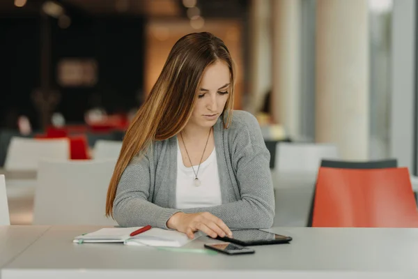 Hübsche Schülerin lernt mit Smartphone und Tablet in einer Highschool-Bibliothek — Stockfoto