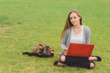 akıllı telefon ve laptop ile çimenlerin üzerinde oturan genç kız