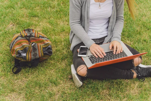 Молодая девушка сидит на траве со смартфоном и ноутбуком — стоковое фото