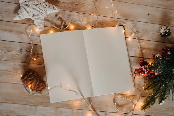 खुली नोटबुक शीट साफ़ करें। प्रकाशों के साथ लकड़ी के डेस्क पर क्रिसमस और नए साल की सजावट का शीर्ष दृश्य — स्टॉक फ़ोटो, इमेज