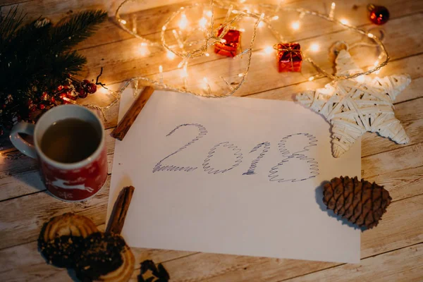 2018 wrtiten auf Papier. Draufsicht auf Weihnachts- und Neujahrsdekorationen auf Holztisch mit Lichtern — Stockfoto