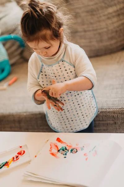 toddler girl in drawing apron draws fingers at home