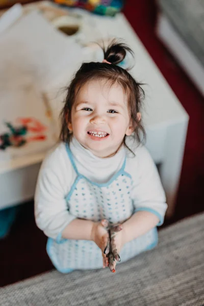 Småbarn flicka i ritning förkläde drar fingrar hemma, leende på — Stockfoto