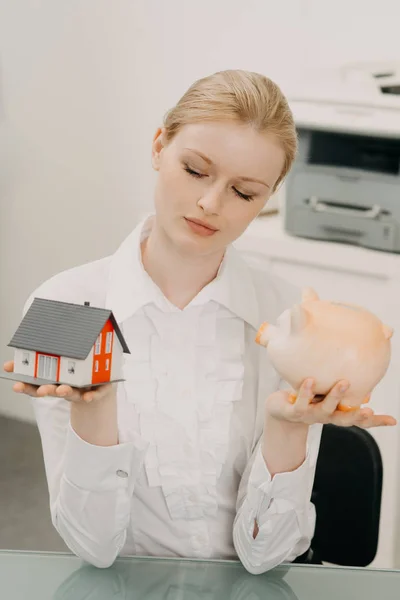 Mooie vrouw in kantoor, bedrijf model van huis en spaarpot. — Stockfoto