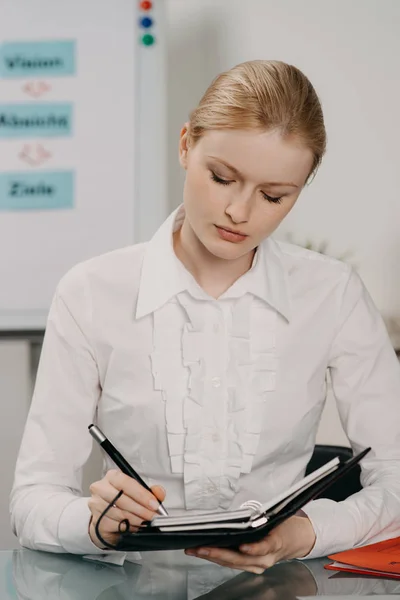 Hermosa mujer en la oficina trabaja en el escritorio, escribiendo en planificador —  Fotos de Stock