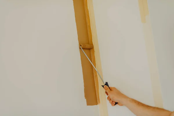 Cerca de las manos de un joven pintando la pared con un rodillo — Foto de Stock