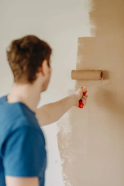 Cerca de las manos de un joven pintando la pared con un rodillo — Foto de Stock