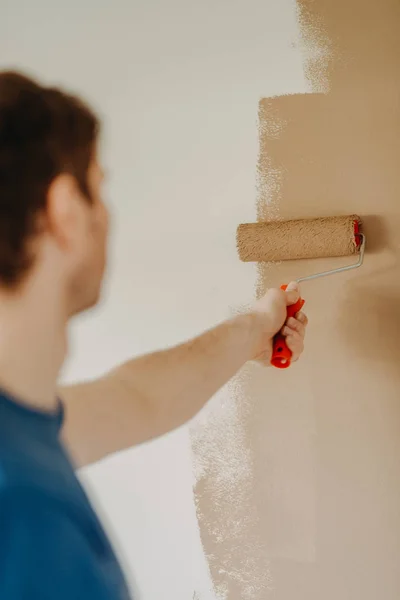 Cerca de las manos de un joven pintando la pared con un rodillo — Foto de Stock