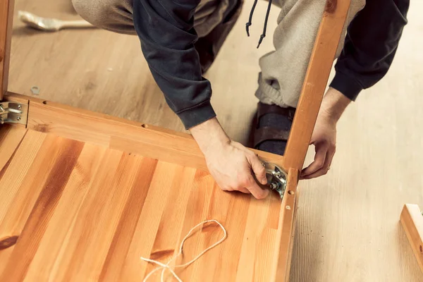 Hombre atornilla las piernas a una mesa de madera — Foto de Stock