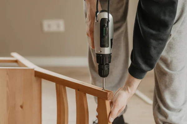 Cerrar las manos del trabajador atornillar la silla con destornillador electrónico —  Fotos de Stock