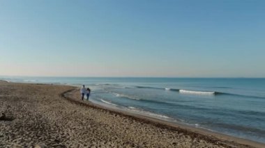 Fiumicino, İtalya. Deniz kenarında el ele tutuşan genç bir çift. Adam ve kız gün doğumunda sahilde dalgaların arka planına karşı yürür. Hava görünümü